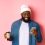 Image of stylish Black man hipster drinking takeaway coffee, reading message on phone and smiling, standing over pink background.